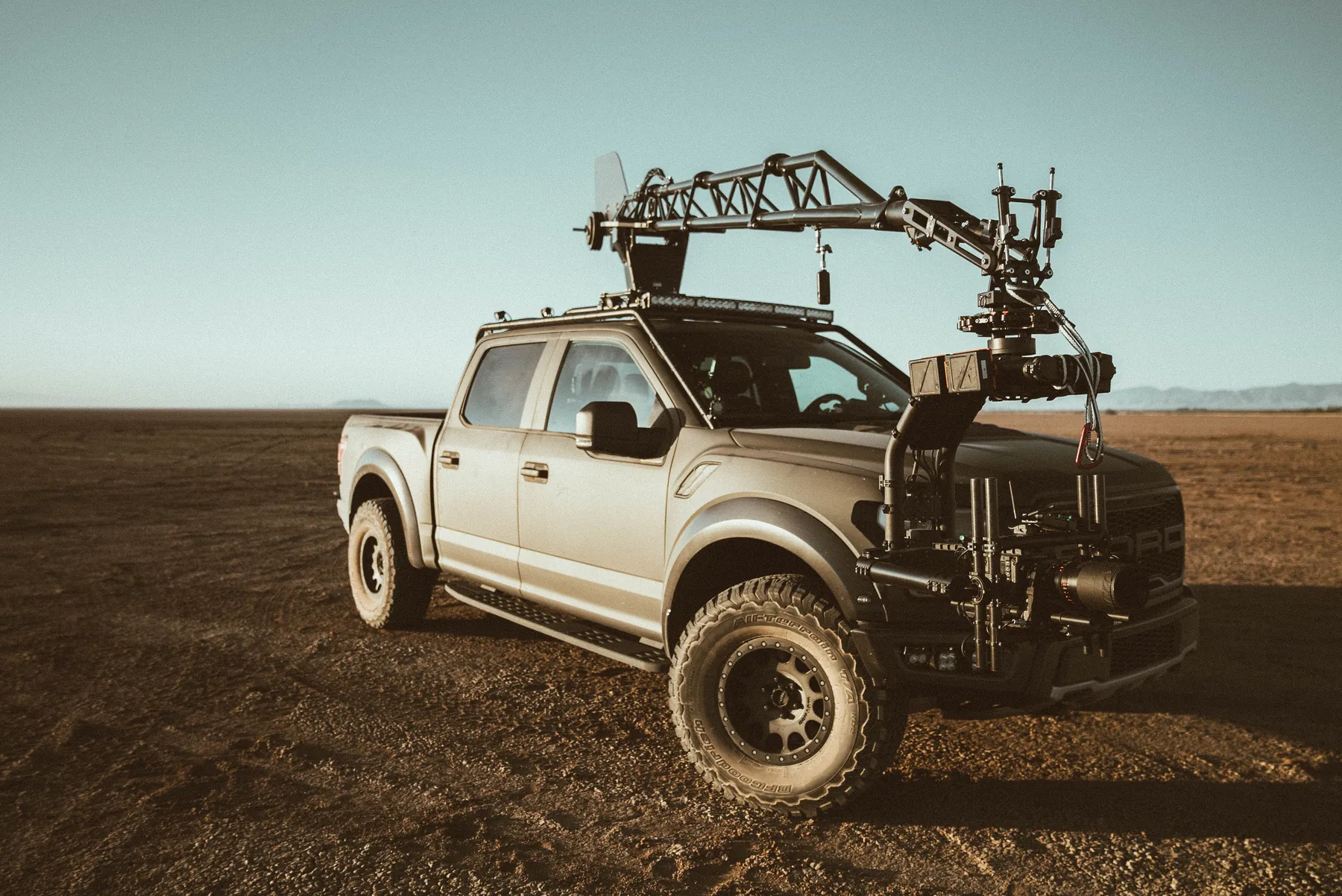 A pickup carrying a camera crane across open ground